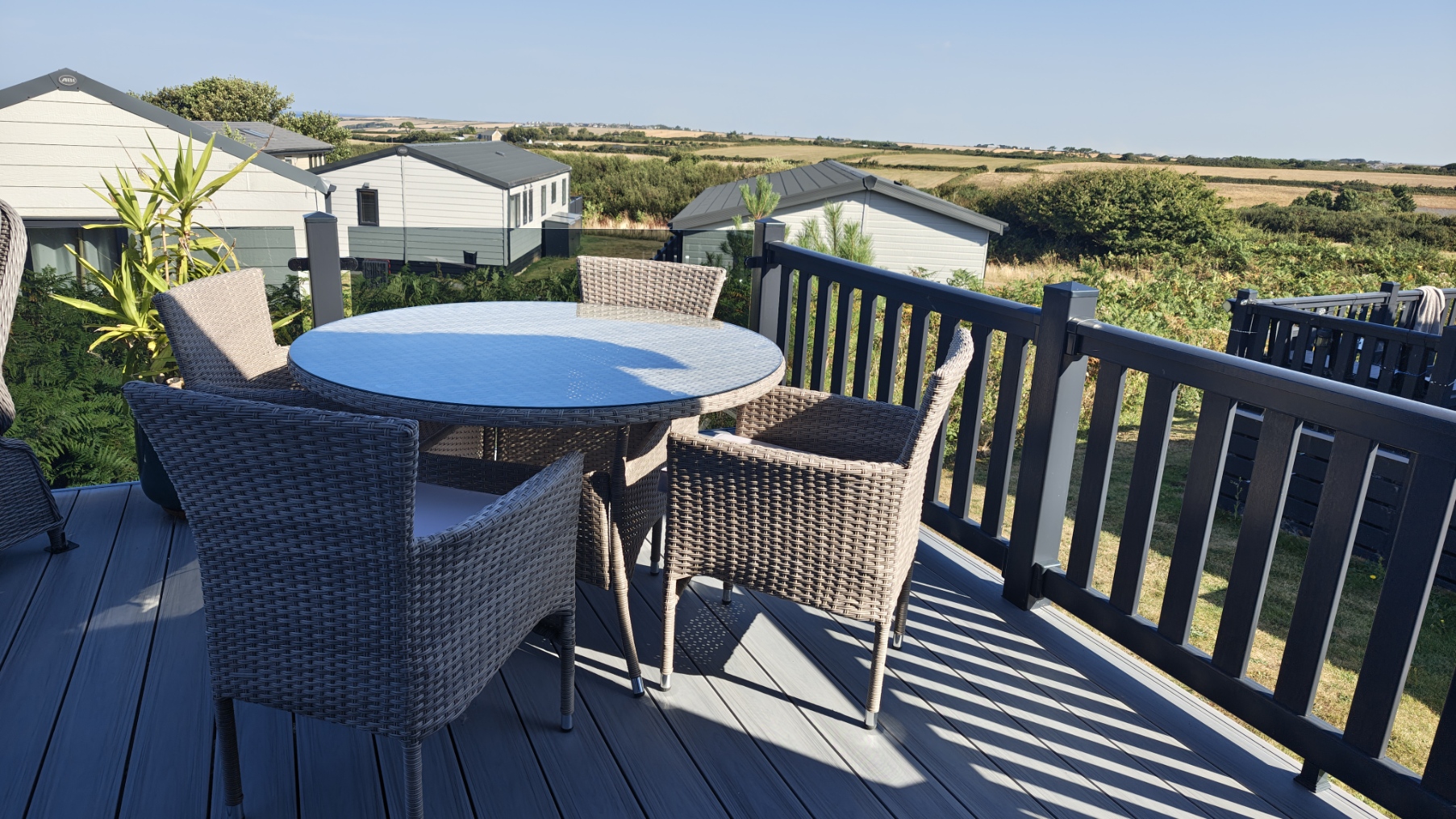 The sunny decking of the lodge, with outdoor dining furniture and views over the Cornish countryside